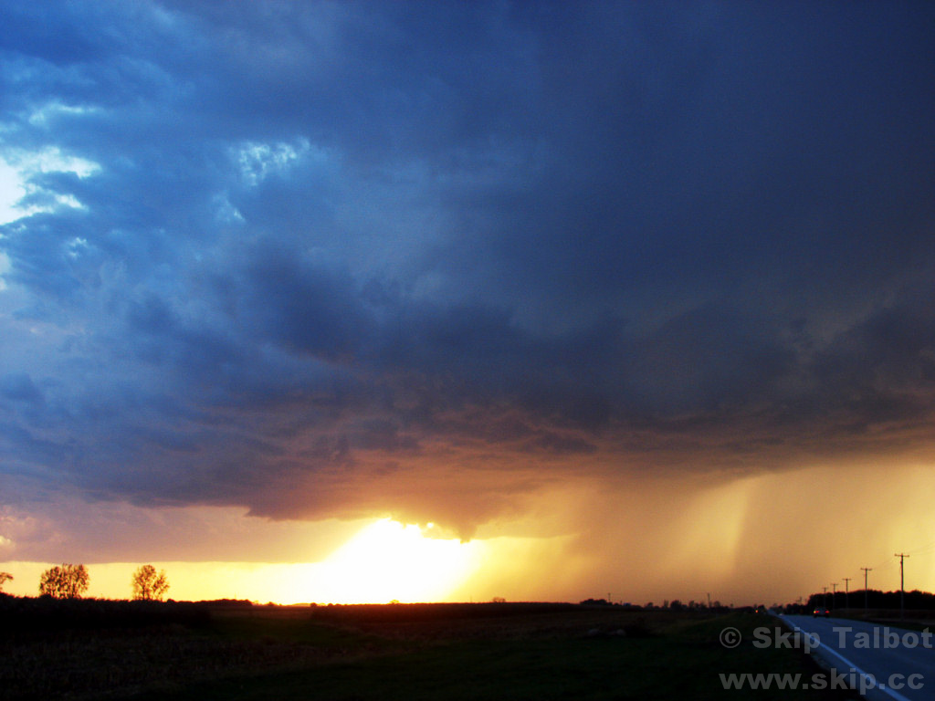 A small thunderstorm illuminated in fiery shades by the setting sun
