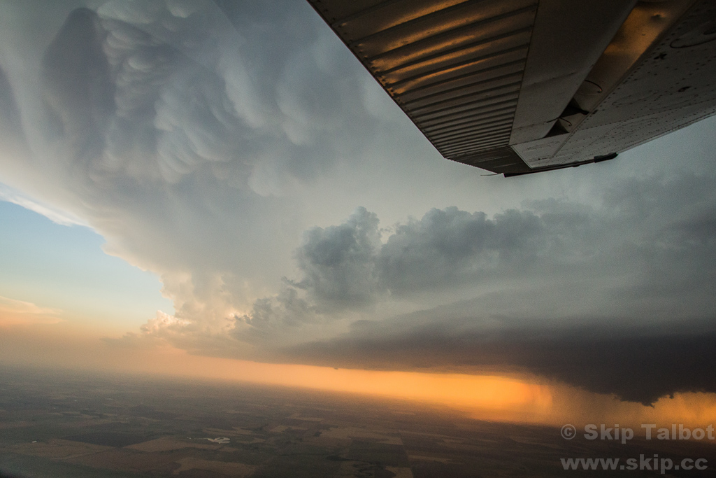 A mammatus studded anvil (top left), updraft tower (center right), and backlit orange wall cloud (bottom right) photographed from the air